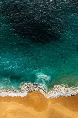 Turkuaz denizi ve dikey manzaralı güzel kumlu bir sahil. Tropikal turkuaz okyanus plajı Nusa Penida Bali Endonezya 'nın insansız hava aracı görüntüsü. Güzel dalgaları olan ıssız kumlu bir sahil. Endonezya plajları.