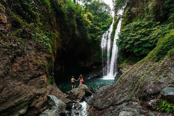 Şelalede aşıklar, dikiz manzarası. Endonezya 'da güzel bir şelaleye hayran olan bir çift. Bali 'de tatilde olan bir çift. Balayı gezisi. Çift Asya 'da seyahat ediyor. Bali adasında tatil.