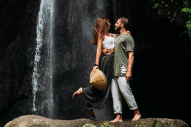 Bir adam şelalede bir kadını kucaklıyor. Şelalede aşık bir çift. Balayı gezisi. Bali 'deki mutlu çift. Birbirlerine aşık güzel bir çift. Aşıklar şelalede kucaklaşır.