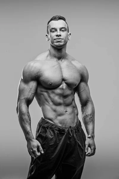 Schwarz-Weiß-Foto eines muskulösen und fitten jungen Fitnessmodels, das vor grauem Hintergrund posiert. — Stockfoto