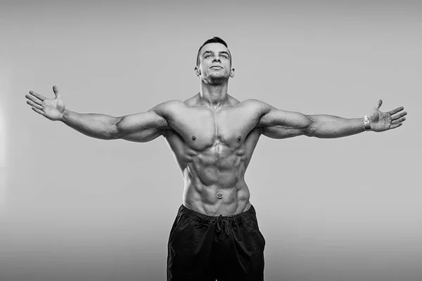 Schwarz-Weiß-Foto eines muskulösen und fitten jungen Fitnessmodels, das vor grauem Hintergrund posiert. — Stockfoto