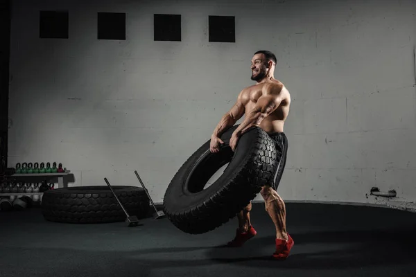 Atletický trénink. Svalnatý muž převracení pneumatiky v tělocvičně — Stock fotografie