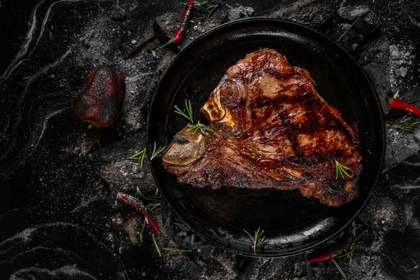 Жареный мясной стейк на черном фоне древесного угля. Сочный стейк с дымом на углях с розмарином. Гриль вкусный маринованный стейк на углях, крупным планом фото . — стоковое фото