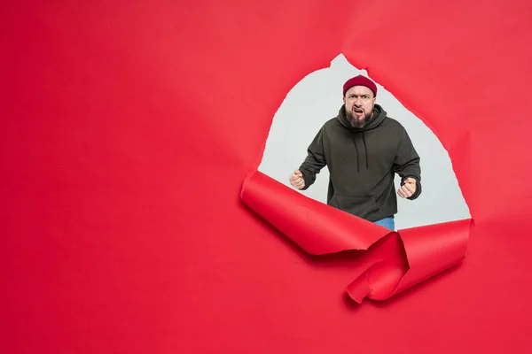 Brutal divertido hombre con una barba detrás de un rojo roto fondo —  Fotos de Stock