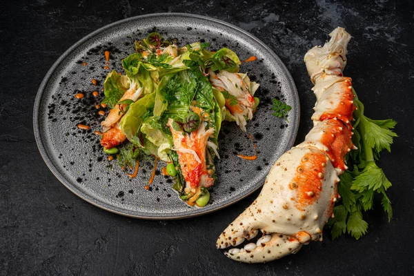 Salad with crab meat on a stone plate and black table.