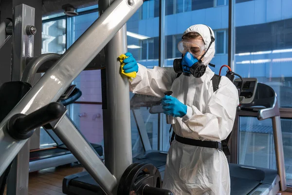 Cleaning and Disinfection in crowded places amid the coronavirus epidemic Gym cleaning and disinfection Infection prevention and control of epidemic. Protective suit and mask and spray bag