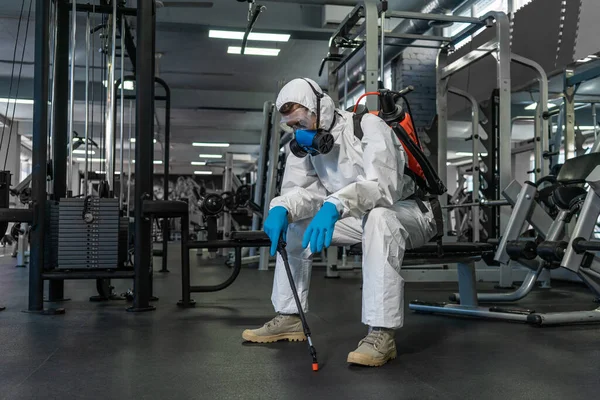コロナウイルス流行中の混雑した場所での清掃と消毒ジムの清掃と消毒感染予防と流行の制御 保護スーツとマスクとスプレーバッグ — ストック写真