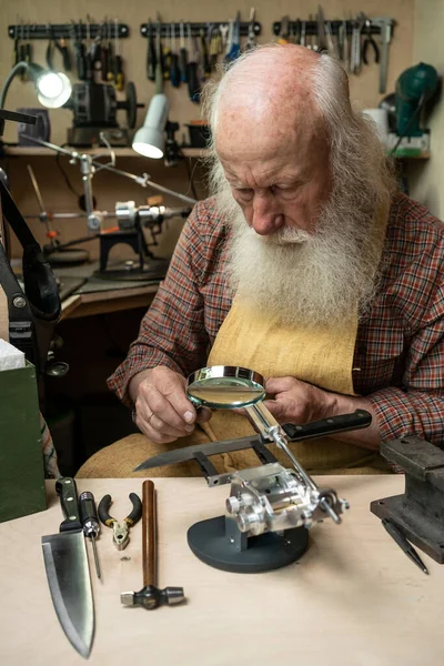 A man looks through a magnifying glass on the cutting edge of the knife to check its sharpening