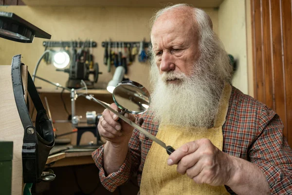 A man looks through a magnifying glass on the cutting edge of the knife to check its sharpening