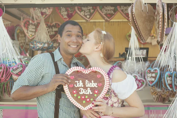 Young man gets a kiss for giving his date a traditional Oktoberfest gingerbread heart Lebkuchenherz — Stock Photo, Image