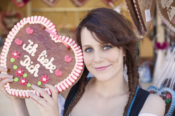 Chica alemana vistiendo un Dirndl y sosteniendo el tradicional corazón de pan de jengibre del Oktoberfest —  Fotos de Stock