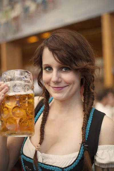 Retrato de la alegre joven alemana vestida con dirndl tradicional y sosteniendo una taza de cerveza dentro de una tienda de campaña en Oktoberfest —  Fotos de Stock