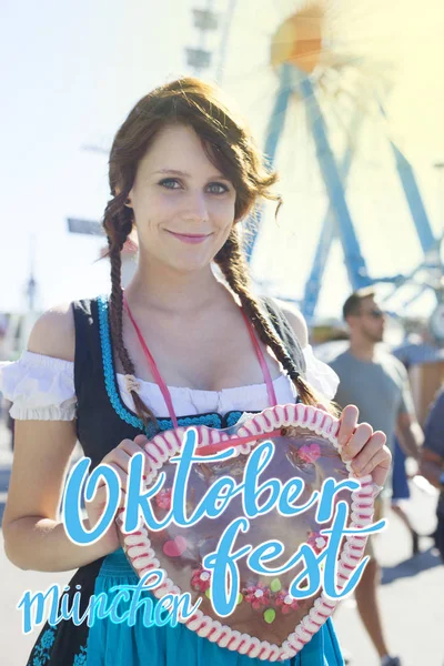 Chica alemana vistiendo un Dirndl y sosteniendo el tradicional corazón de pan de jengibre del Oktoberfest —  Fotos de Stock