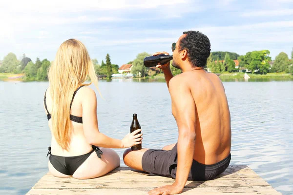 Giovane coppia che beve una birra vicino ad un lago — Foto Stock