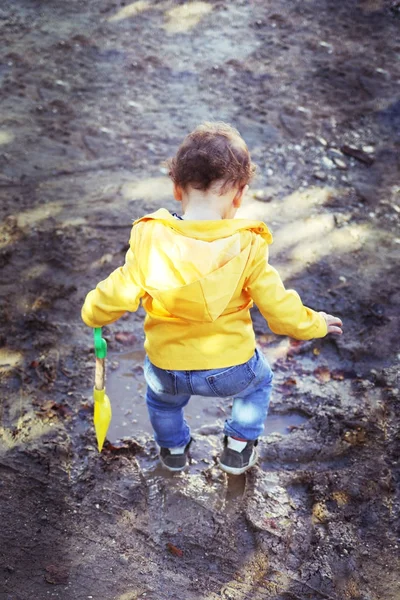 Copil în jachetă de ploaie galbenă sărind peste baltă — Fotografie, imagine de stoc