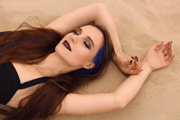 Fiatal lány, hosszú haj, fekete-fehér ruha a homokban fekve közelről portréja. — Stock Fotó