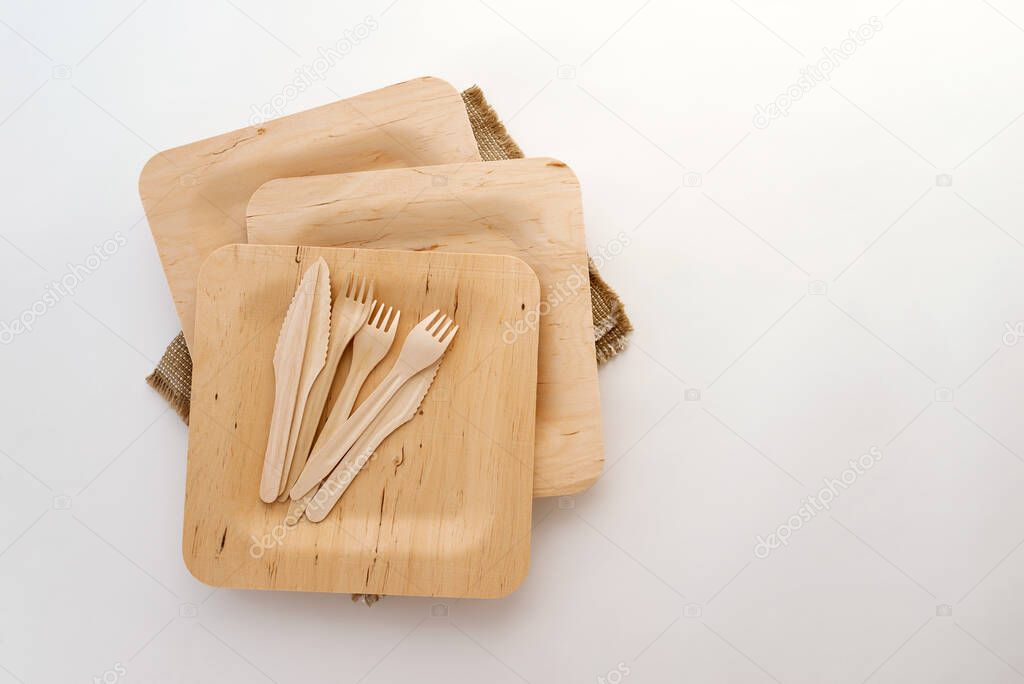 Wooden disposable tableware-plates, knives, forks on a white background, zero waste. Flat lay