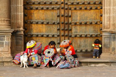 Cusco, Peru - 31 Mart 2019. Geleneksel kostümlü Perulu kadınlar bebek lama ve bir çocuk büyük tahta bir kapının önünde oturuyorlar..
