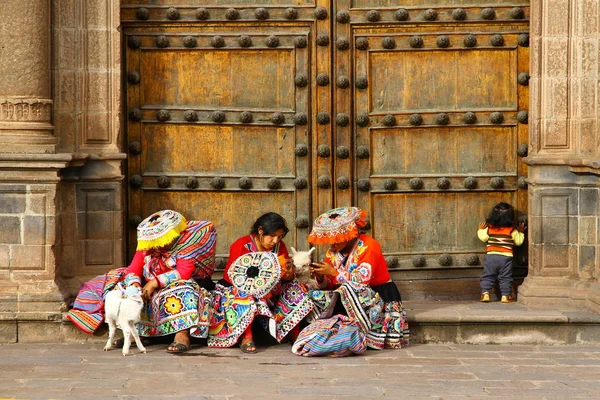 ペルーのクスコ 3月2019 赤ちゃんラマと子供を持つ伝統的な衣装でペルーの女性は巨大な木製のドアの前に座っています — ストック写真