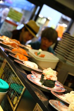 TOKYO, JAPON - 19 Mayıs 2013. Asakusa bölgesindeki suşi restoranının manzarası. Taşıma bandında suşi tabakları çalışıyor ve insanlar sevdiklerini seçebiliyorlar..