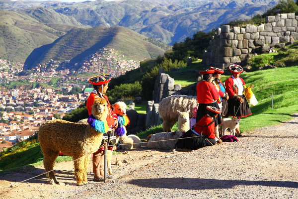 SACSAYHUAMAN FORTRESS, CUSCO, PERU - 28 March 2019. Peruvian women in traditional costumes with their llamas are waiting at the entrance of Sacsayhuaman fortress to take pictures with tourists.