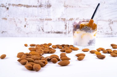 Beyaz zemin üzerinde Chia pudingi, yoğurt, reçel, meyve, kurabiye ve bademlerden oluşan vejetaryen bir çöl.