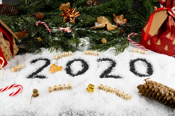 Un arreglo con "2020" escrito en la nieve en el frente, buenos deseos como la paz, la suerte, el amor, la alegría y un feliz año nuevo además. La parte posterior está decorada con abetos, regalos, cañas de azúcar — Foto de Stock