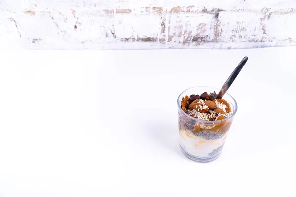 Un deșert vegan din budincă de chia, iaurt, gem, fructe, prăjituri și migdale pe fundal alb — Fotografie, imagine de stoc