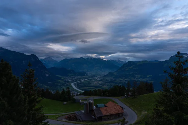 A mountain range and a green hill with some trees under a dramatic sky — 스톡 사진