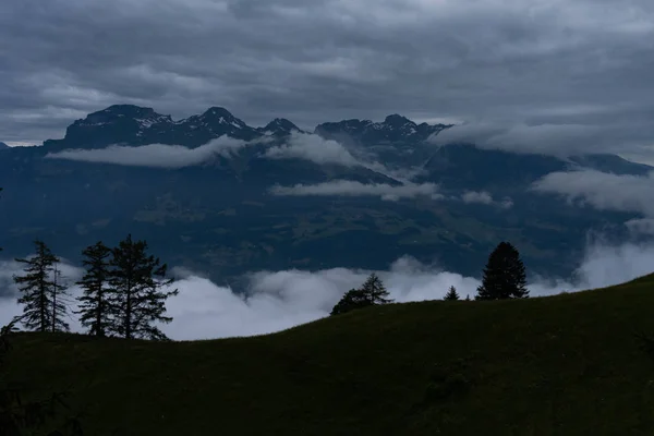 A hill in the front, clouds and a mountain range in the back — 스톡 사진