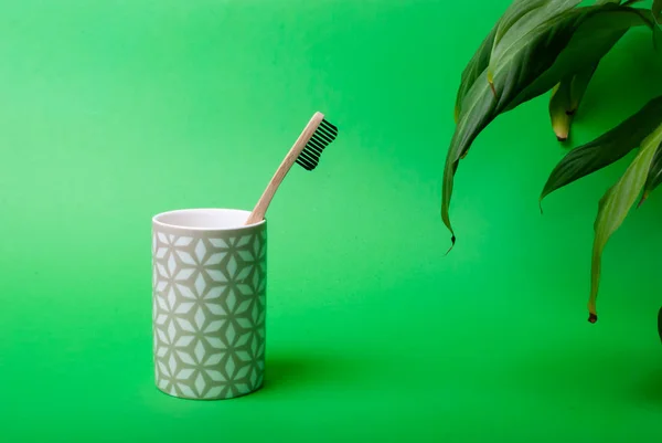 Un cepillo de dientes de bambú en una taza con algunas hojas sobre fondo verde — Foto de Stock