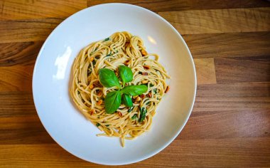 Tahta bir masada duran, beyaz bir tabakta, vejetaryen spagettisi.