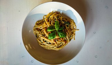 Beyaz bir tabakta, beyaz ahşap bir masada duran, vejetaryen spagetti.