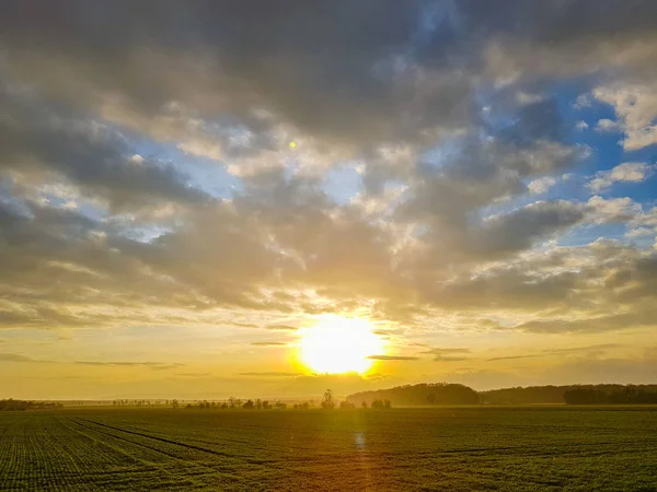 Pôr do sol no céu nublado sobre um campo verde, montanhas na parte de trás — Fotografia de Stock