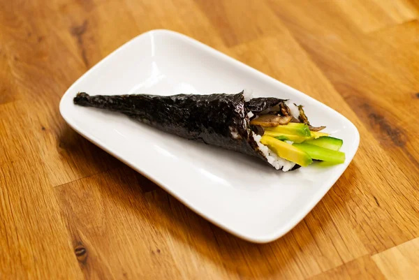 Zelfgemaakte veganist Temaki-Sushi gevuld met avocado op een klein bord op een houten tafel — Stockfoto