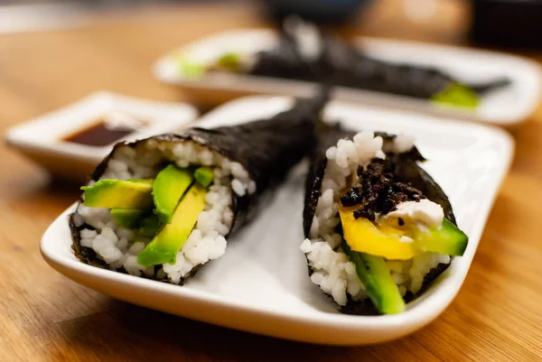 Temaki-Sushi vegan de casă umplut cu avocado pe o farfurie mică pe o masă de lemn cu sos de soia și wasabi — Fotografie, imagine de stoc