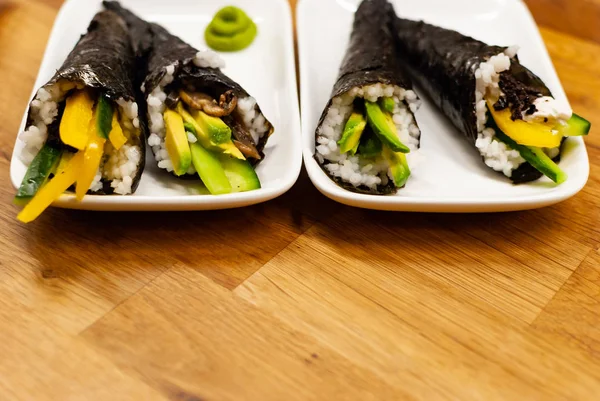 Temaki-Sushi vegan de casă umplut cu avocado pe o farfurie mică pe o masă de lemn cu sos de soia și wasabi — Fotografie, imagine de stoc