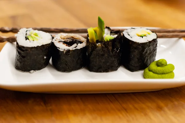 Role vegane de sushi de casă umplute cu avocado pe o farfurie mică pe o masă de lemn cu sos de soia, wasabi și ghimbir — Fotografie, imagine de stoc