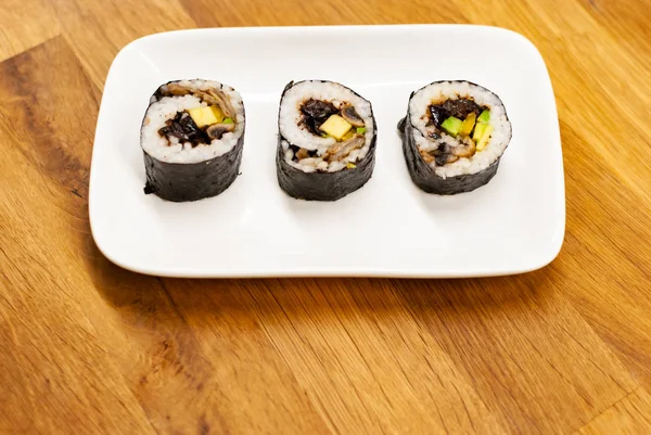 Role vegane de sushi de casă umplute cu avocado pe o farfurie mică pe o masă de lemn cu sos de soia, wasabi și ghimbir — Fotografie, imagine de stoc