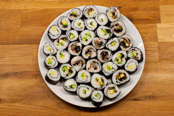 Homemade vegan Sushi rolls filled with avocado on a plate on a wooden table
