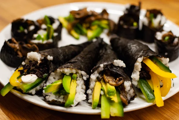 Temaki-Sushi vegan de casă umplut cu avocado pe o farfurie mică pe o masă de lemn cu sos de soia și wasabi — Fotografie, imagine de stoc