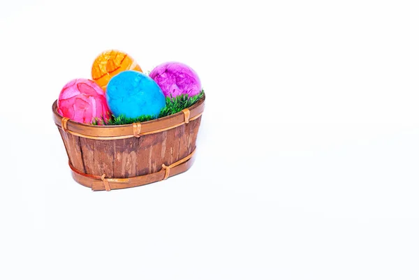 Uma cesta cheia de grama verde e ovos de páscoa coloridos no fundo branco com espaço de cópia — Fotografia de Stock