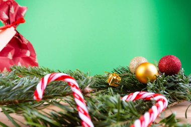 Yeşil köknar dalları ve noel süsleri (noel takıları, şeker kamışları, hediyeler, köknar konisi) yeşil bir arkaplanda, fotokopi alanı olan ahşap bir masa üzerinde