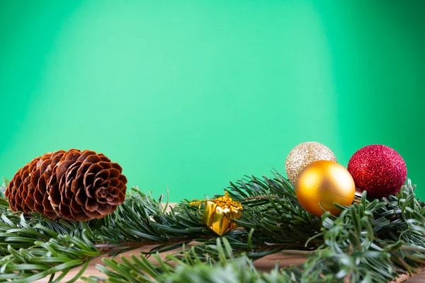 Ramas de abeto verde con adornos navideños (adornos navideños, bastones de caramelo, regalos, cono de abeto) sobre una mesa de madera frente a un fondo verde con espacio para copiar — Foto de Stock