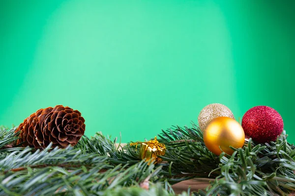 Ramas de abeto verde con adornos navideños (adornos navideños, bastones de caramelo, regalos, cono de abeto) sobre una mesa de madera frente a un fondo verde con espacio para copiar — Foto de Stock