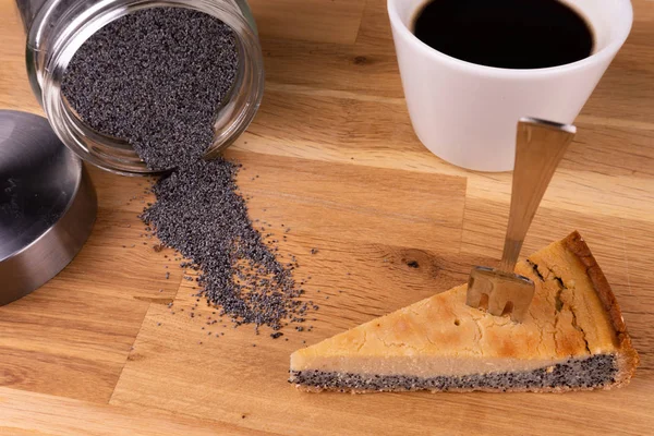 Un morceau de gâteau au fromage végétalien avec des graines de pavot avec une fourchette, une tasse de café et des graines de pavot sur une table en bois — Photo