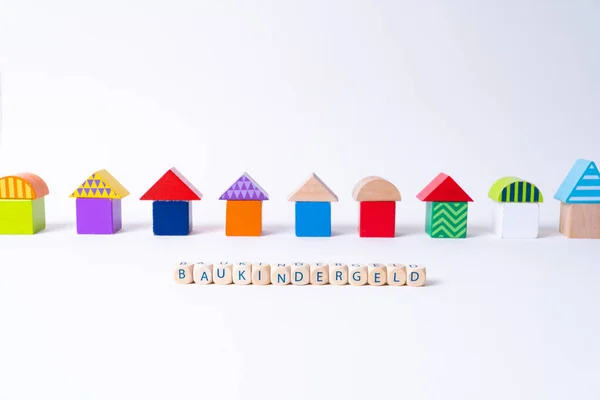 Cubes with letters saying "Baukindergeld", the German word for money for building a house for families in front of a row of houses built of toy colorful toy blocks — Stockfoto