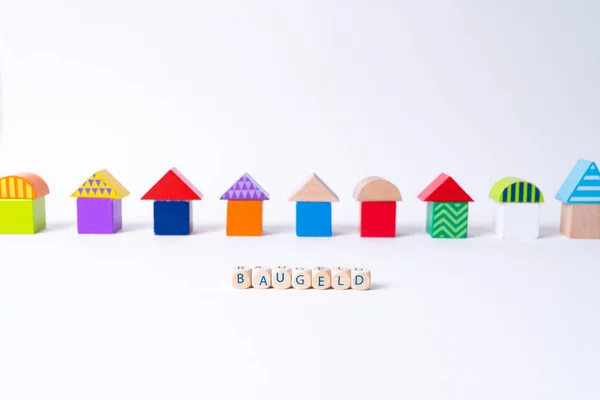 Cubes with letters saying "Baugeld", the German word for money for building a house in front of a row of houses built of toy colorful toy blocks — Stockfoto