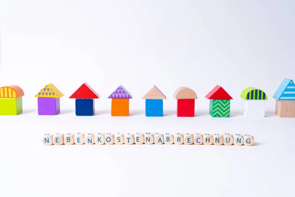 Cubes with letters saying "Nebenkostenabrechnung", the German word for additional costs invoice in front of a row of houses built of toy colorful toy blocks ストックフォト