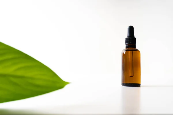 A small bottle with a dropper full of CBD oil or any other oil and a green leaf on white background — 스톡 사진